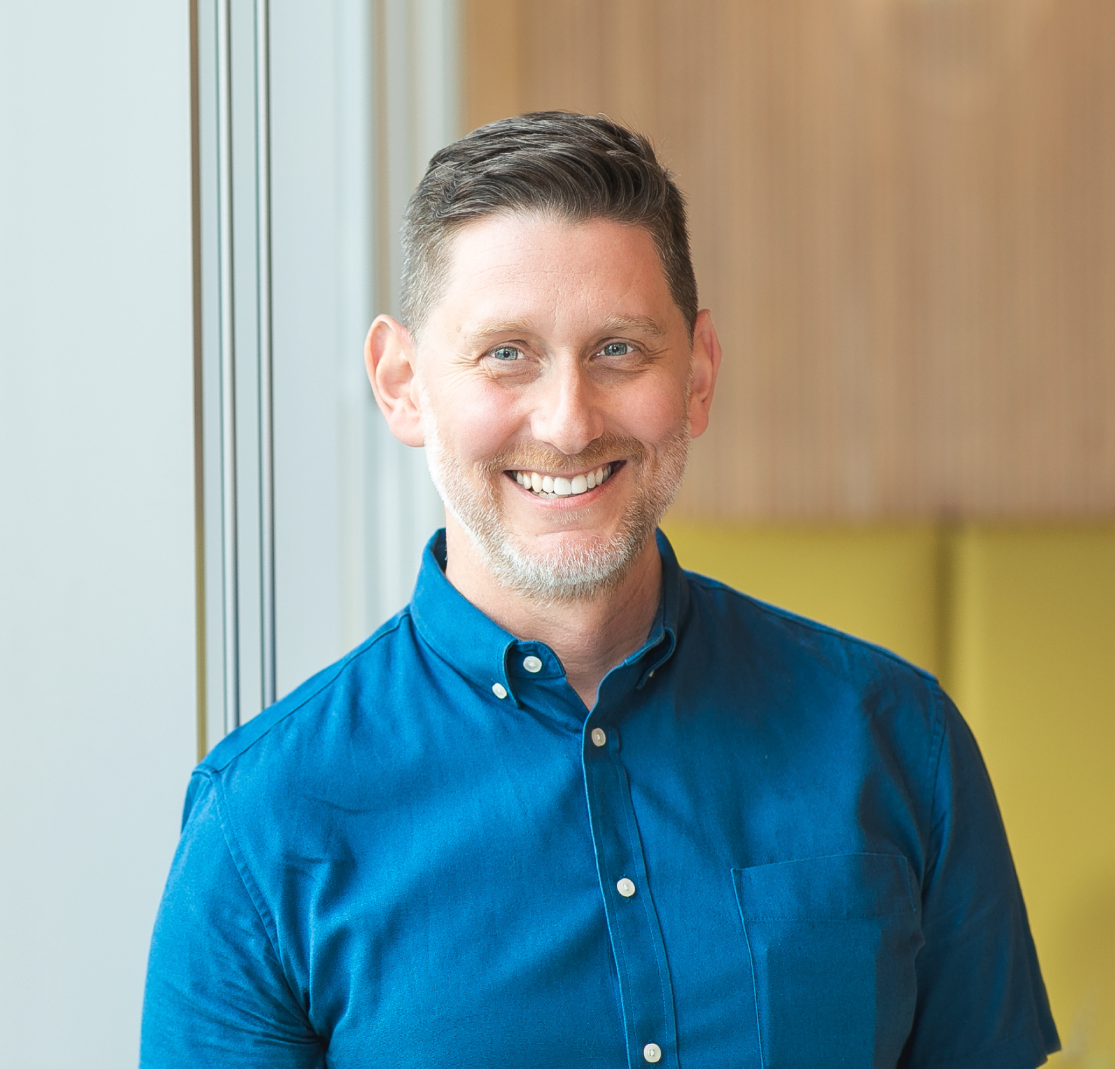 Jarren smiles naturally at the camera in this portrait; he has blue eyes, a warm smile, and a bright blue shirt.
